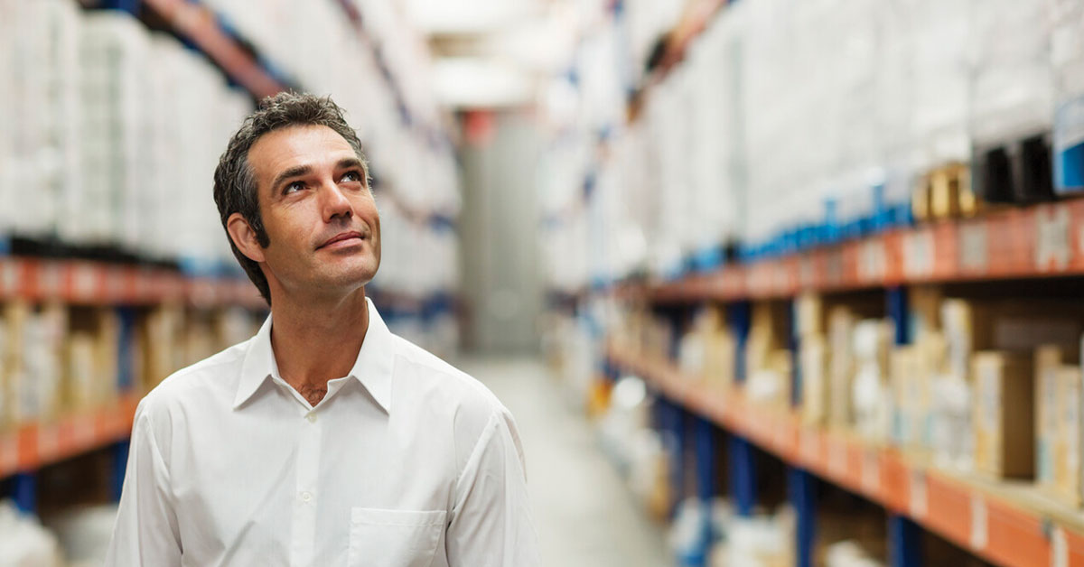 Smiling supervisor looking at stock arranged on shelves in warehouse