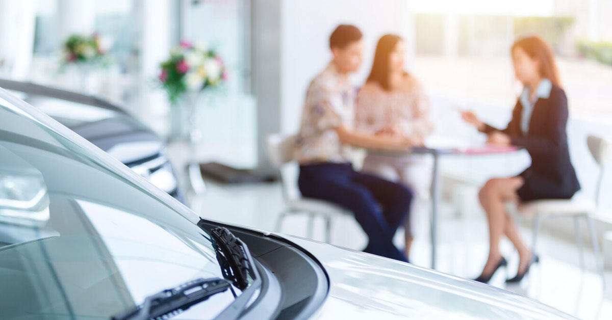 Selective focus on a new car and blur the dealership professional salesman and couple purchasing brand new car.