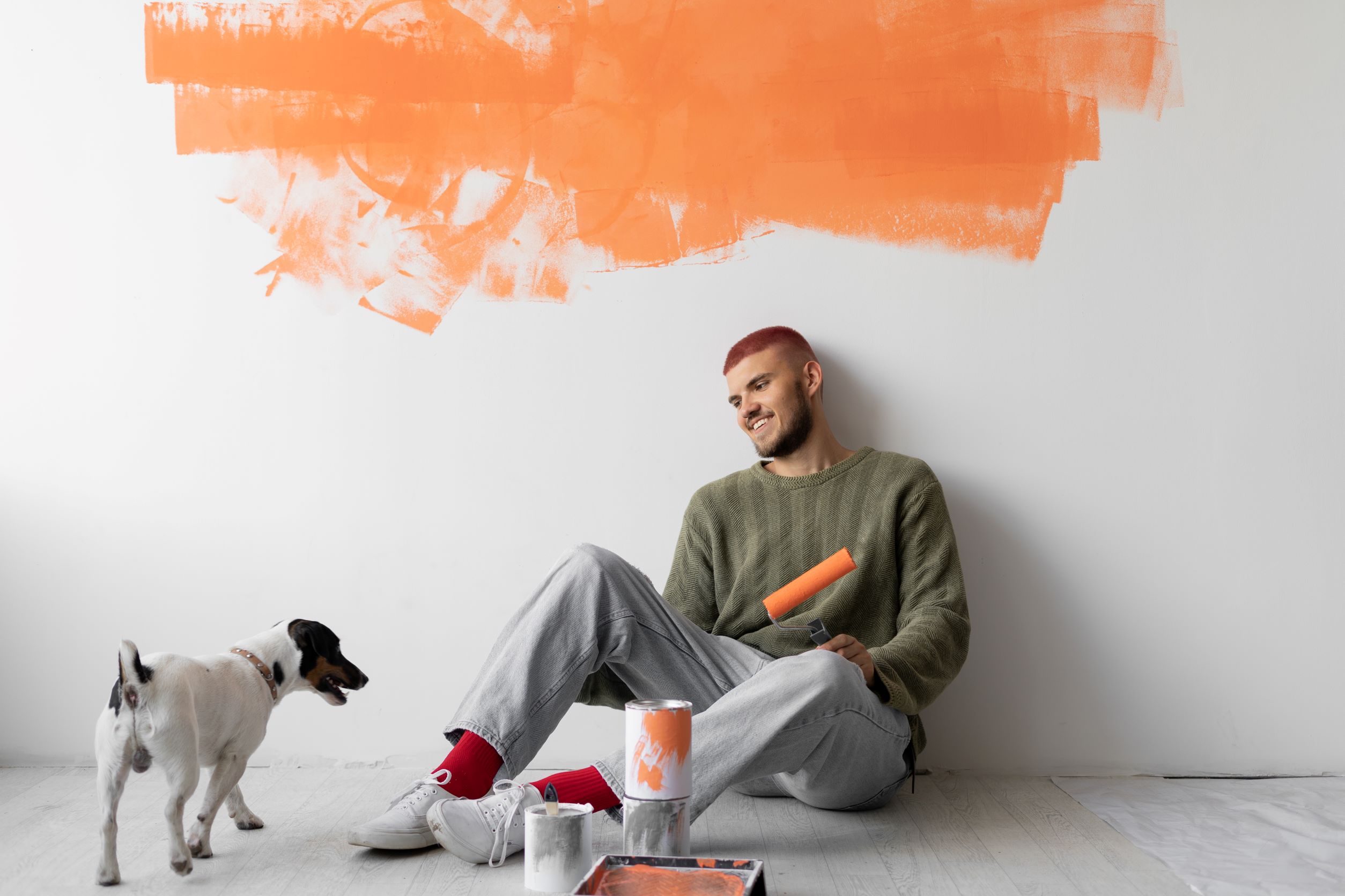 Man seating down holding a paint roller and looking at his dog